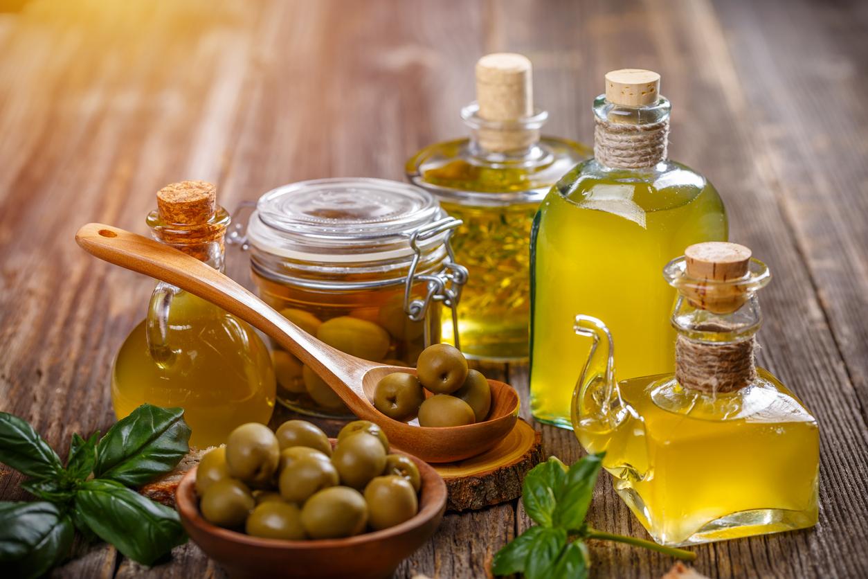 Bottles of olive oil are pictured beside a bowl of olives atop a wooden table.